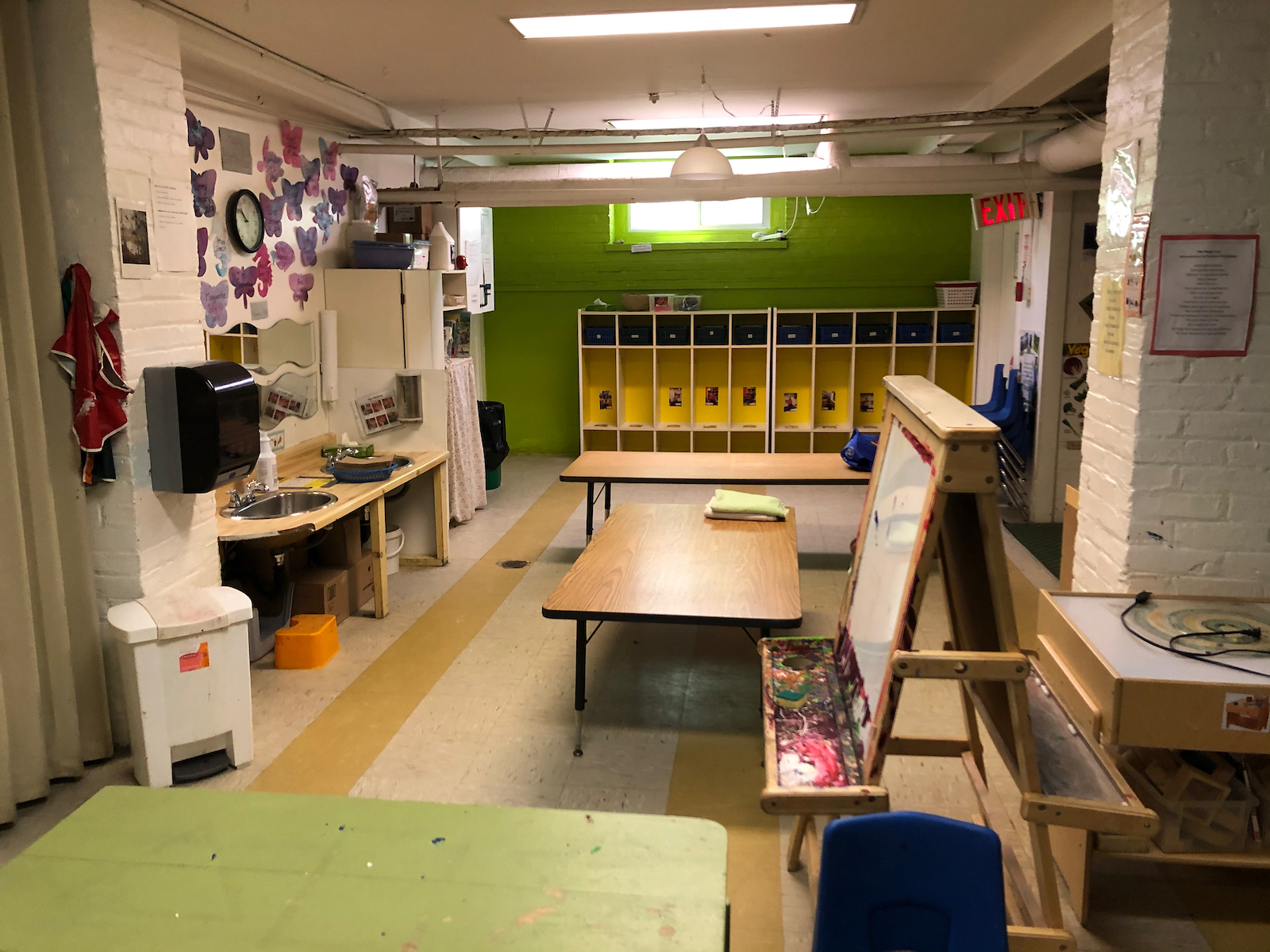 Classroom with cubbies in the far wall, two child-sized sinks on the left and an easel on the right